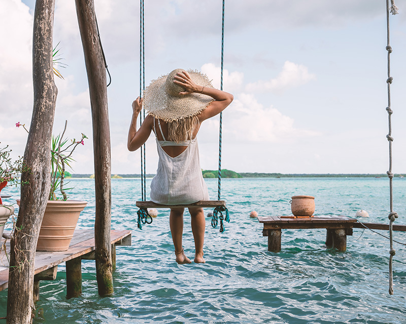 Woman in a hat swinging over the ocean on a beautiful day, feeling good about life after nurse coaching services with Body of Grace Living